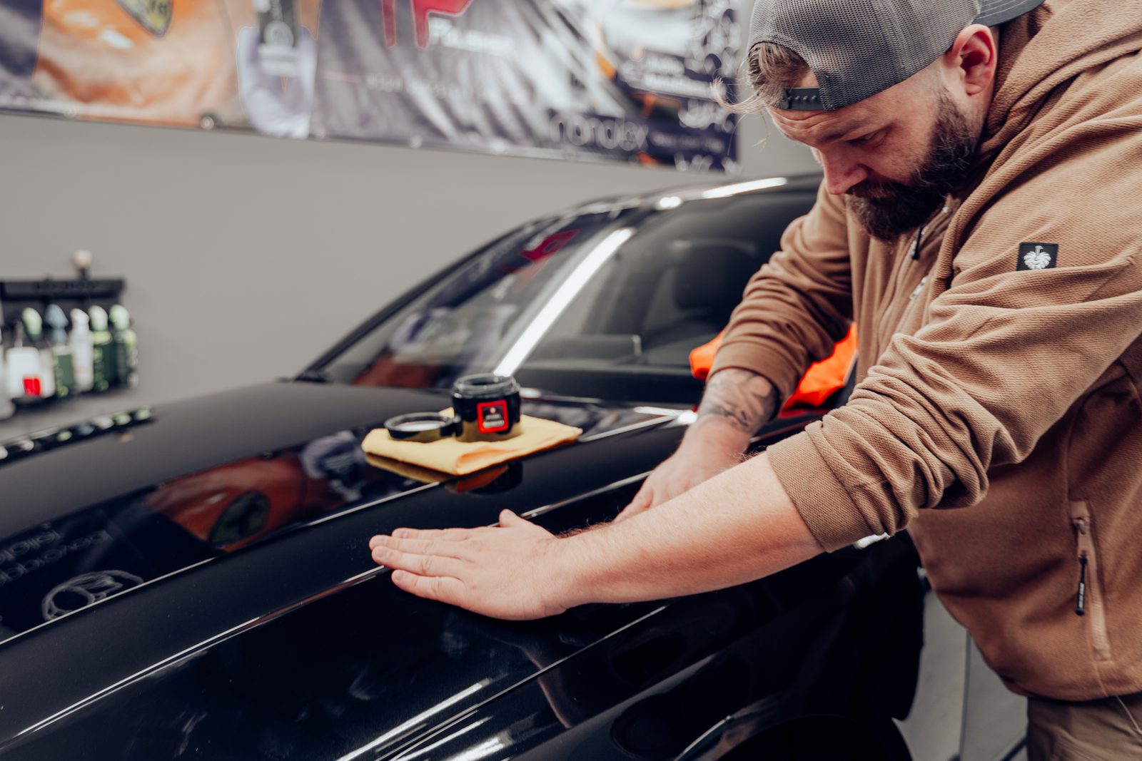 Stefan trägt Wachs von Hand auf die Motorhaube eines schwarzen Sportwagens auf