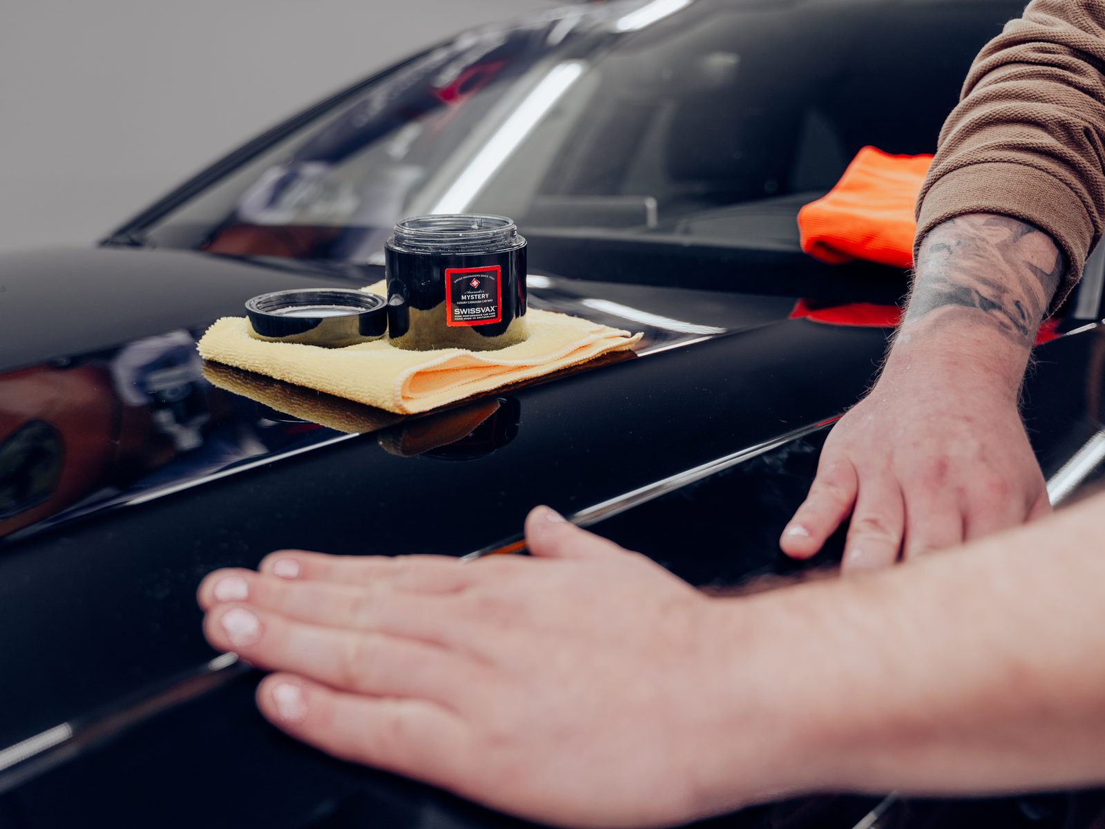Swissvax Carnaubawachs wird von Hand auf eine schwarze Motorhaube aufgetragen