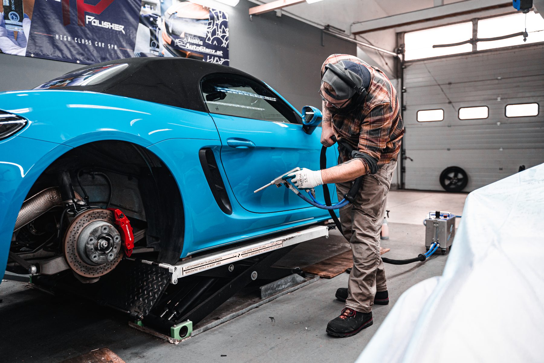 Trockeneisreinigung an der Seitenlinie eines blauen Porsche Roadsters auf der Hebebühne